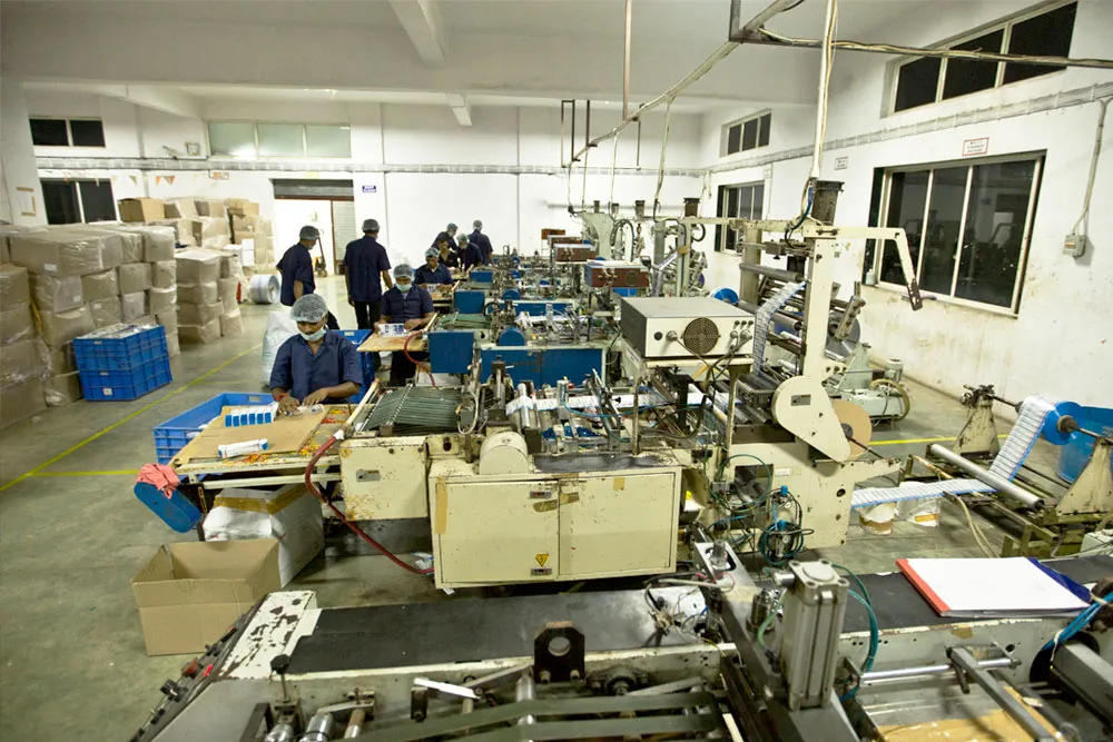 Converting hall with a row of machines, operators at the benches and cartons stacked along the wall