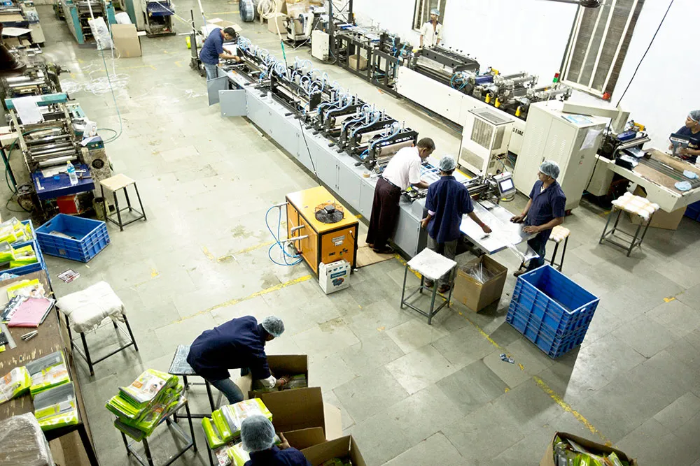 Operators in caps and masks working an automated converting line beside stacked crates of finished stock